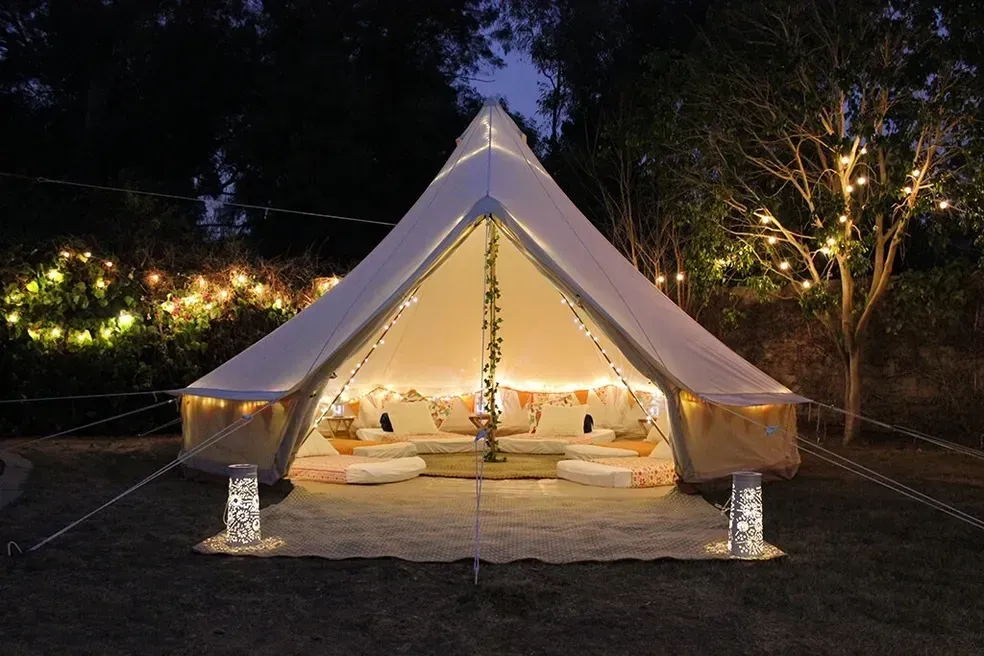A tent with a lot of pillows inside of it is lit up at night.