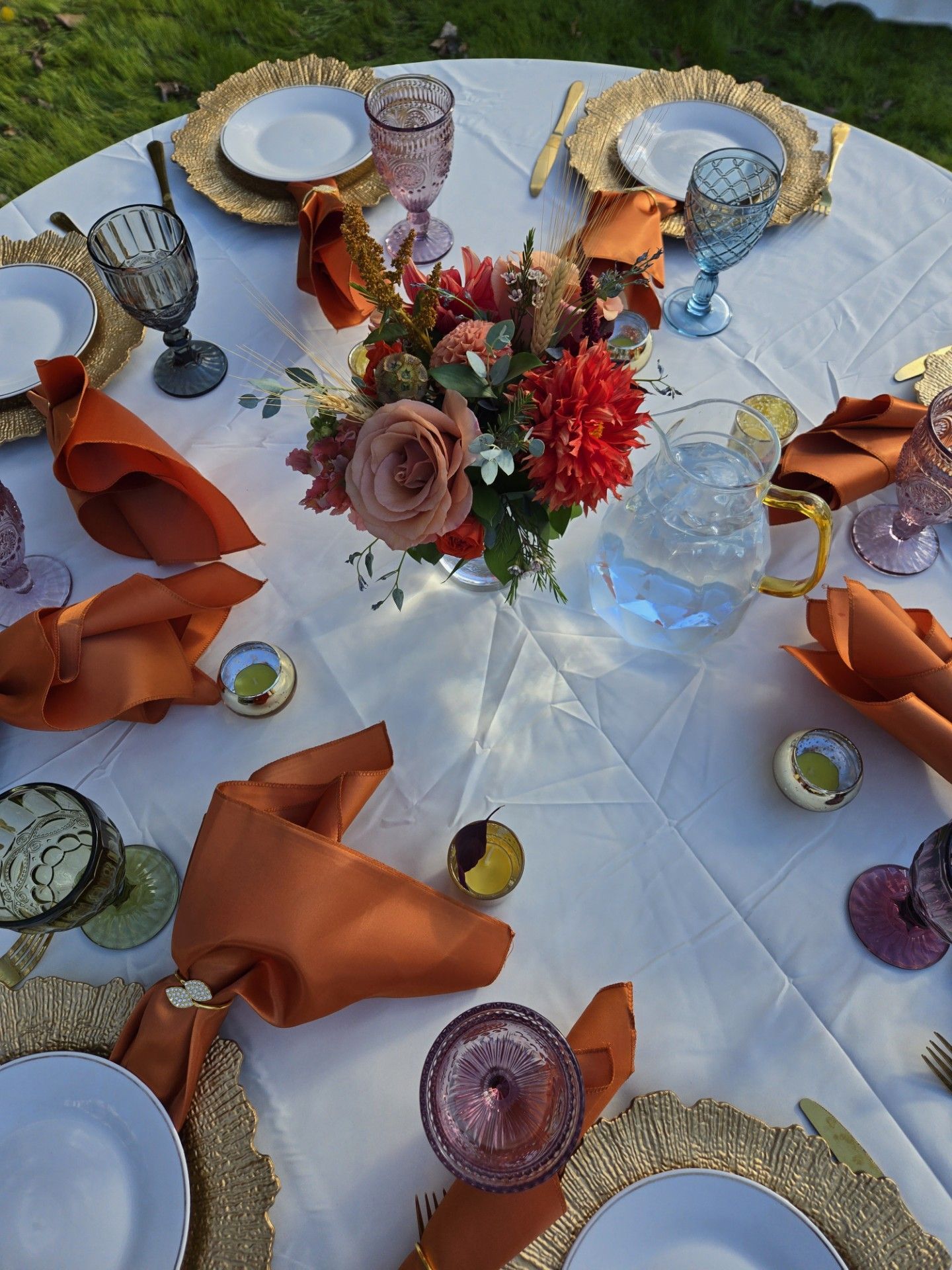 A table with plates , glasses , napkins and a vase of flowers on it.