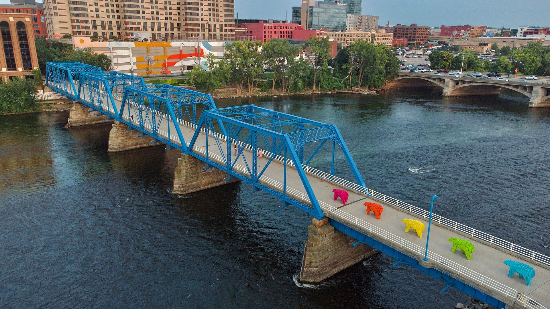 Blue pedestrian bridge with colorful sculptures in Grand Rapids.
