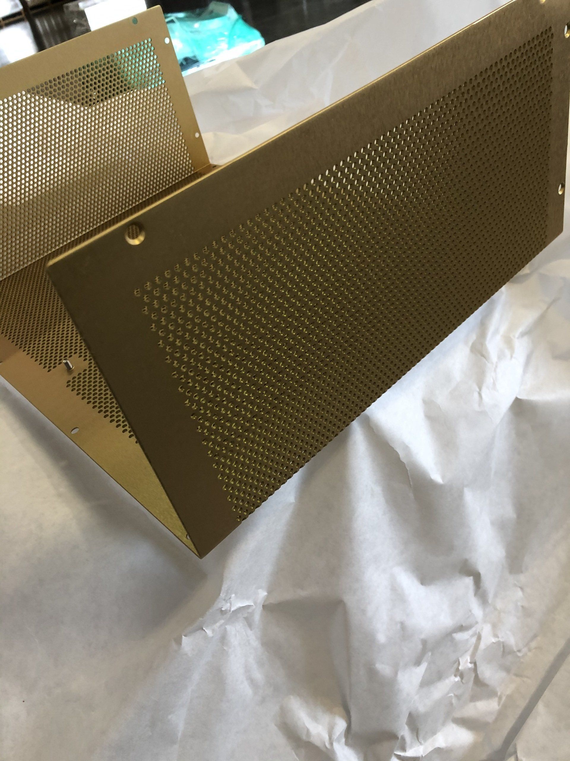 Two gold-colored, perforated metal panels, likely ventilation covers, on crumpled white paper.