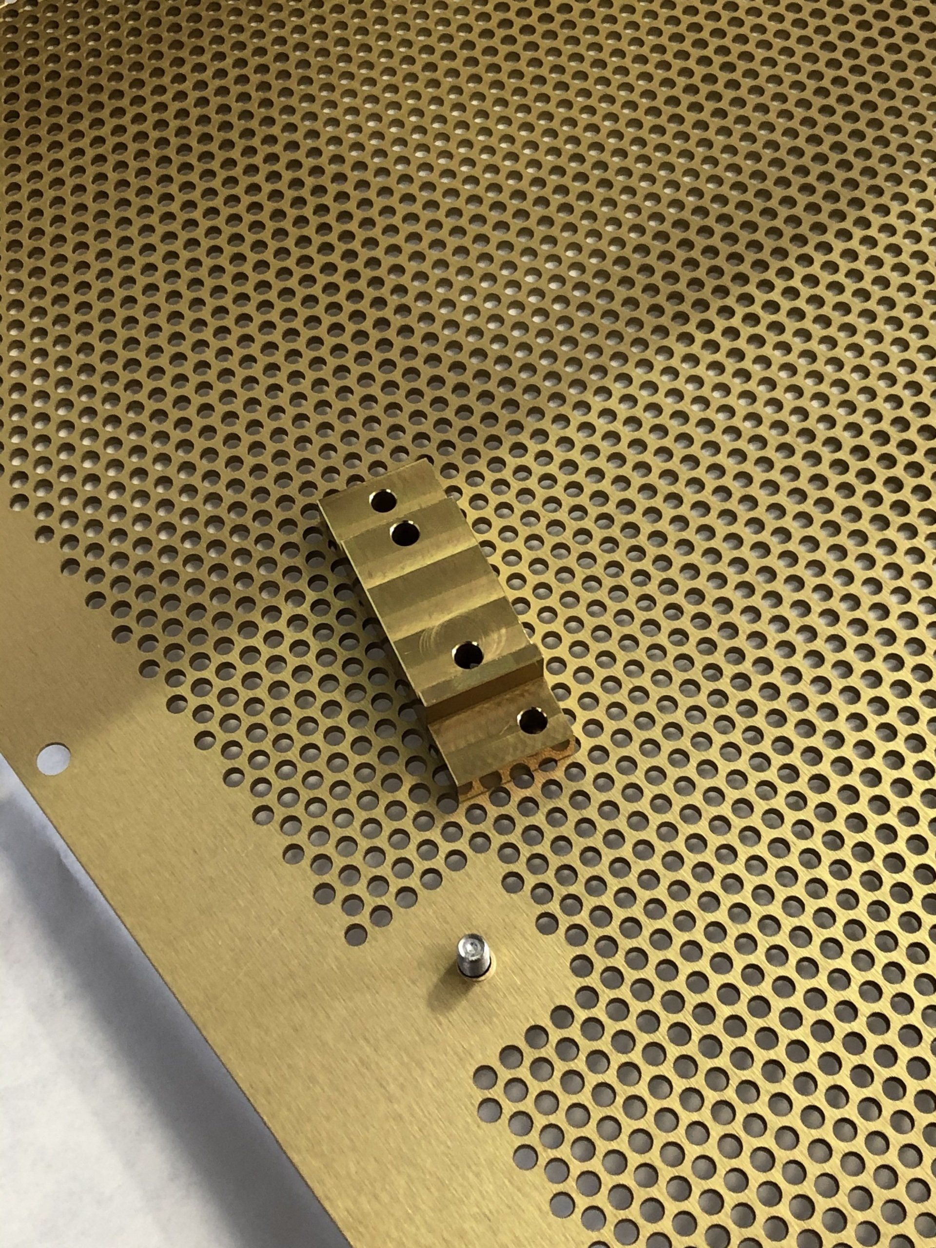Brass perforated sheet with a small, stepped brass component and a screw.