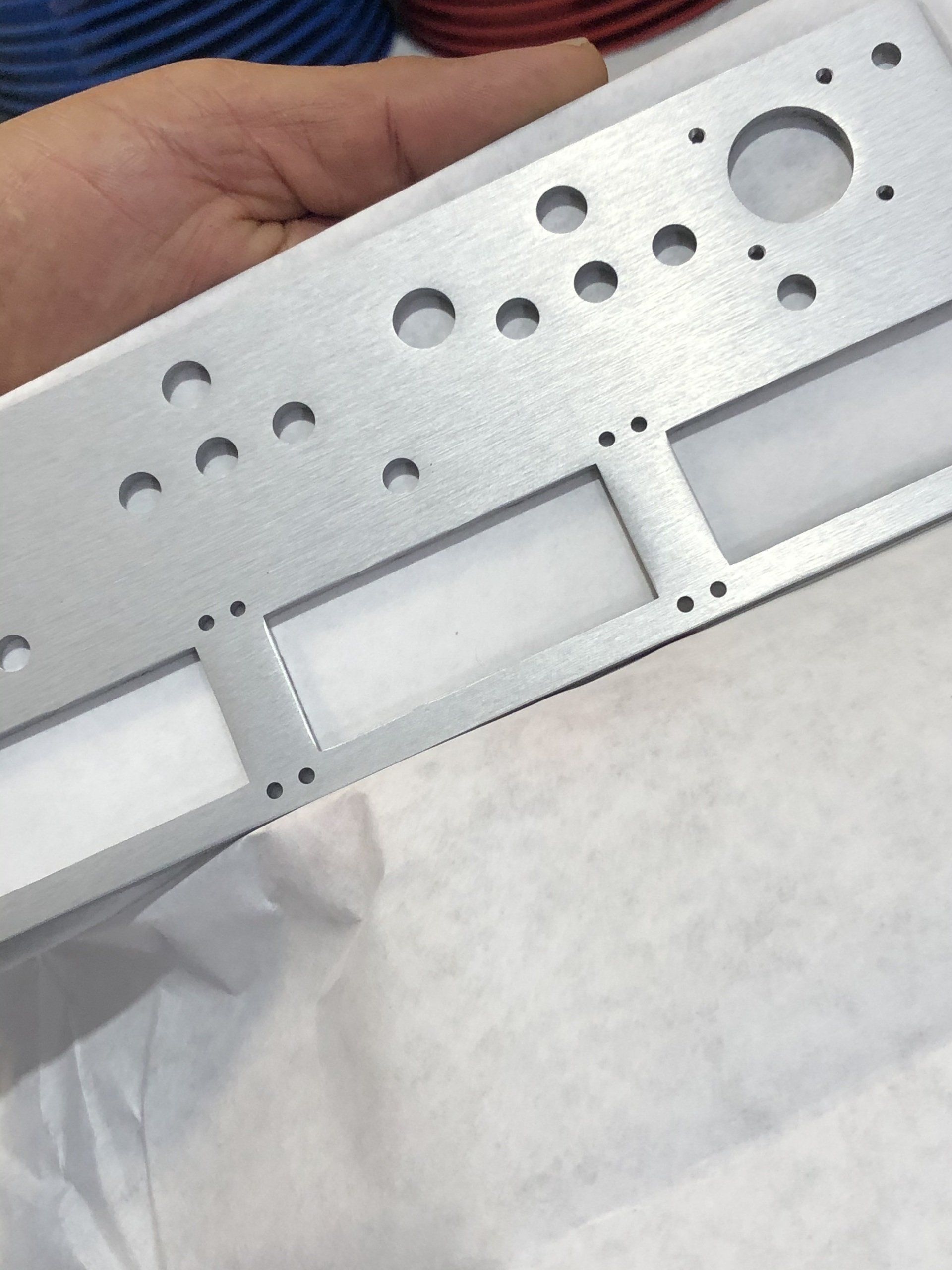 Hand holding a silver metal panel with various holes and cutouts, likely for electronic components.