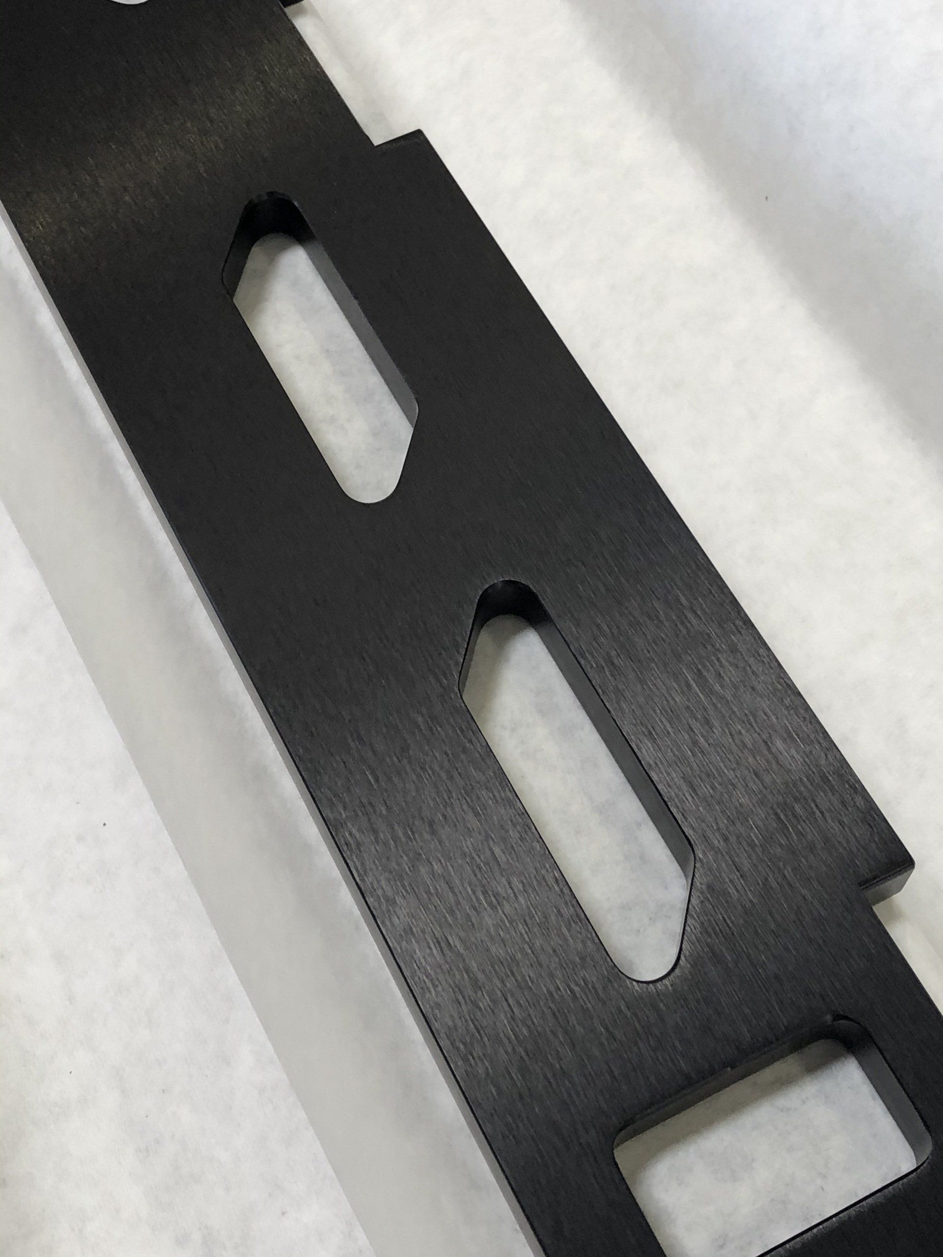 Black metal bracket with three cut-out holes, lying on a white surface.