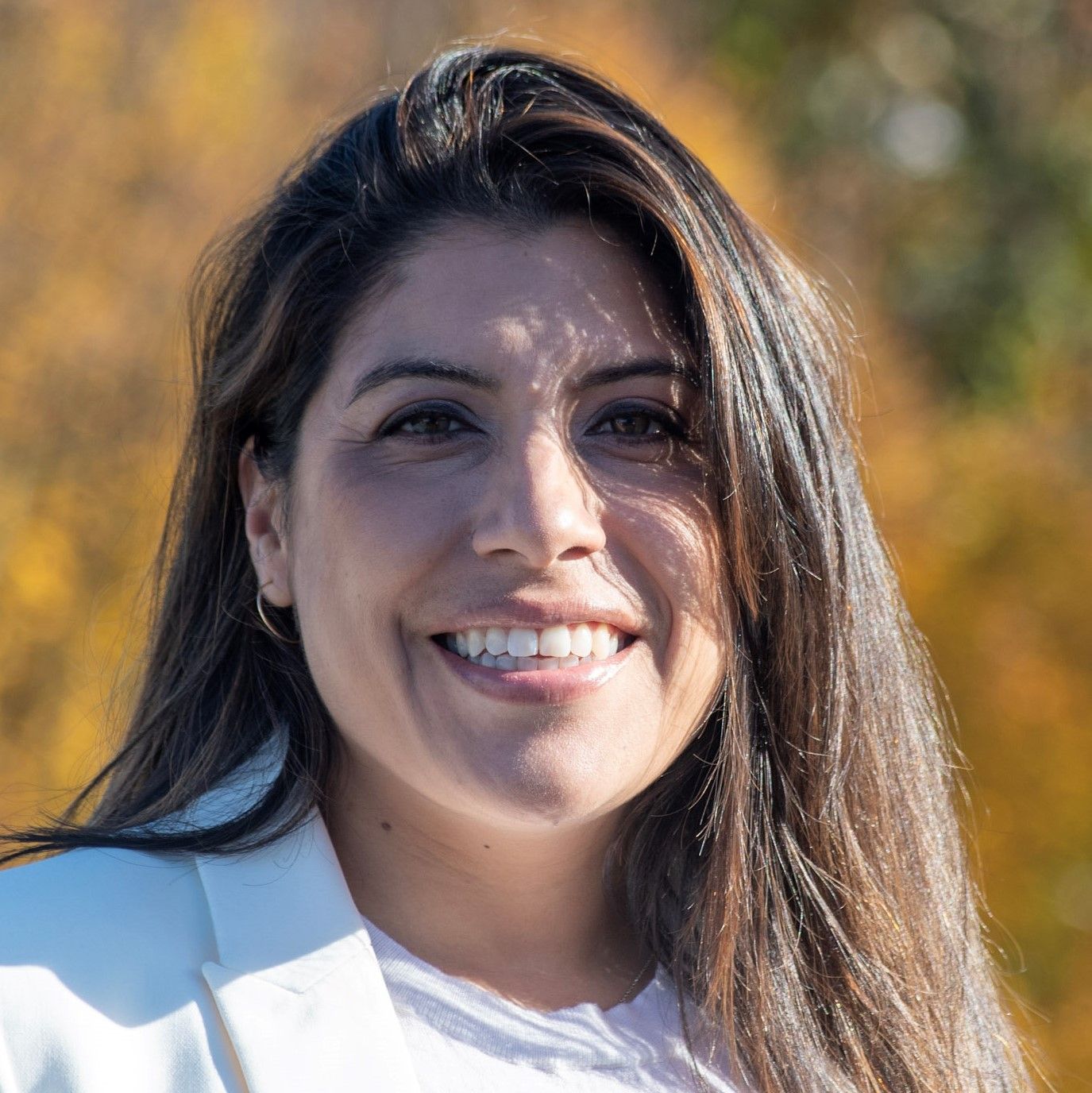 A woman with long hair is smiling for the camera while wearing a white jacket.