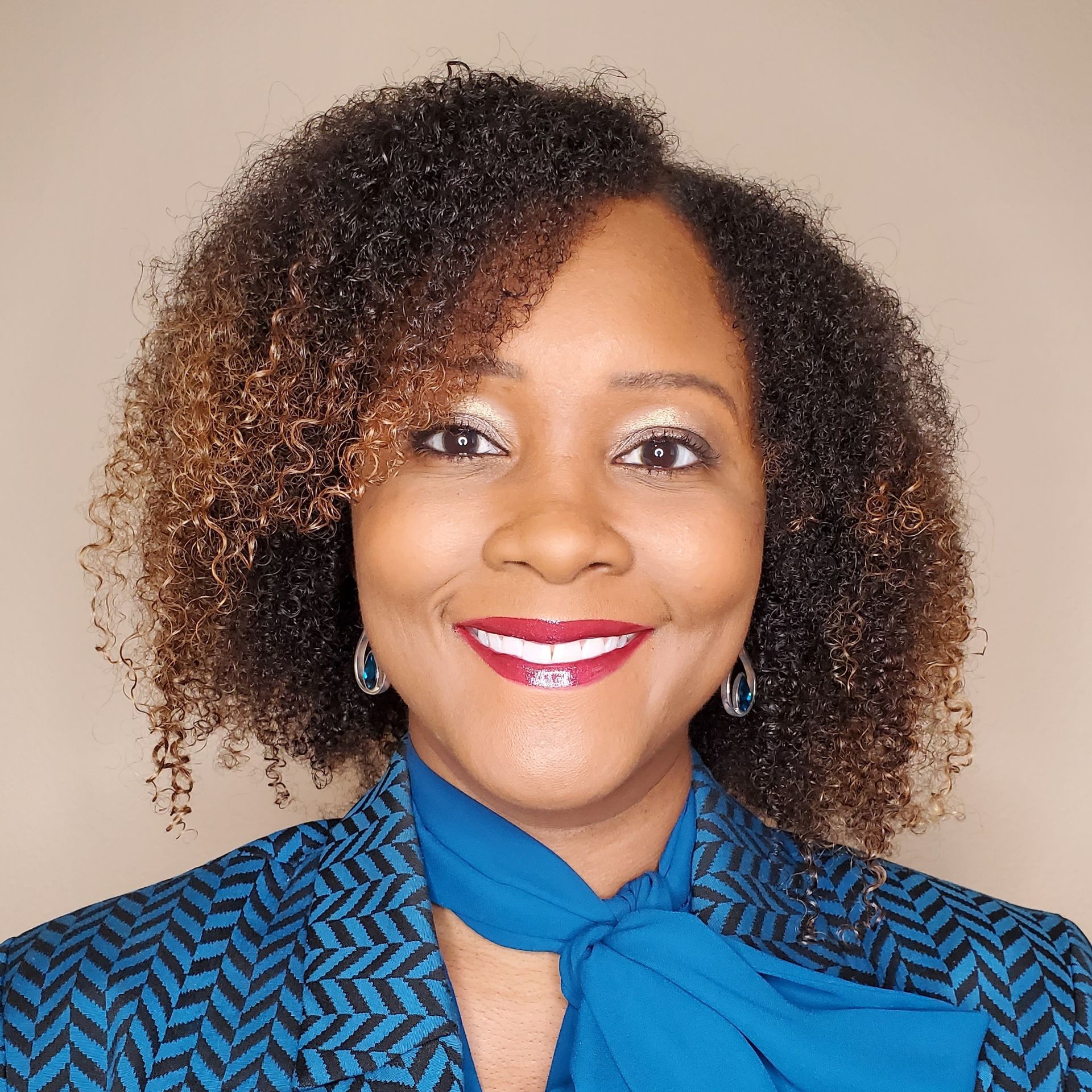 A woman with curly hair is wearing a blue jacket and a blue tie.