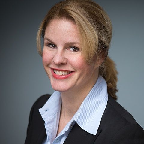 A woman in a suit and blue shirt is smiling for the camera