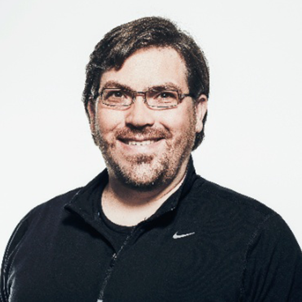 A man wearing glasses and a black nike jacket smiles for the camera