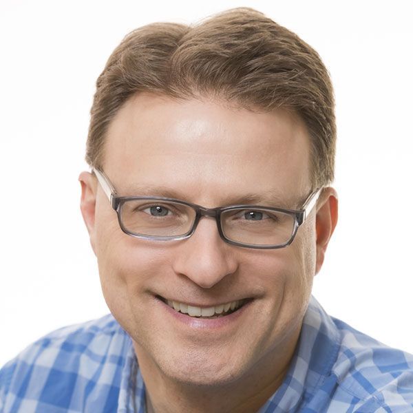 A man wearing glasses and a plaid shirt smiles for the camera