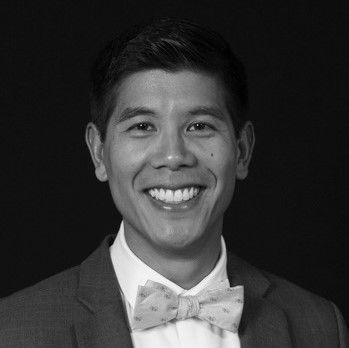 A man in a suit and bow tie is smiling in a black and white photo.