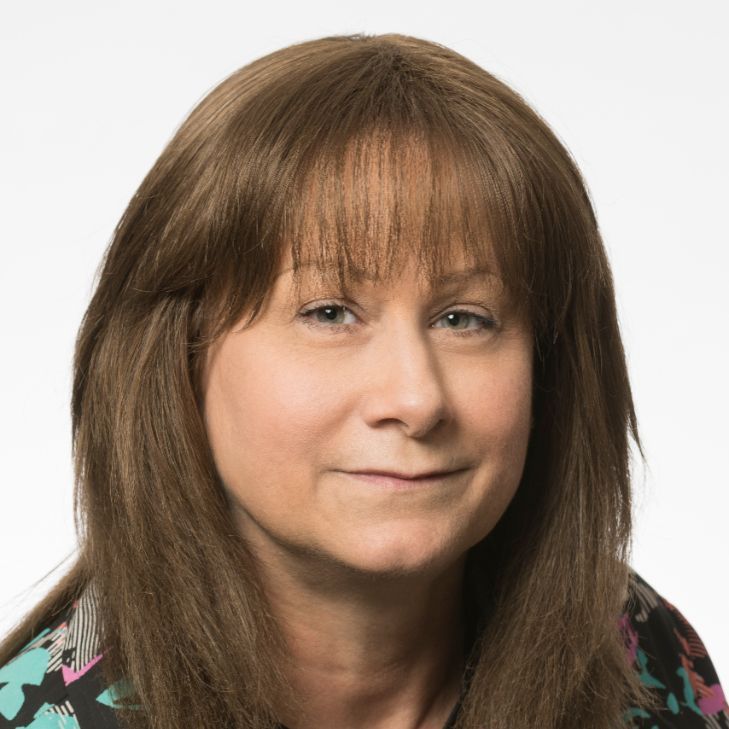 A woman with long brown hair and bangs is smiling for the camera