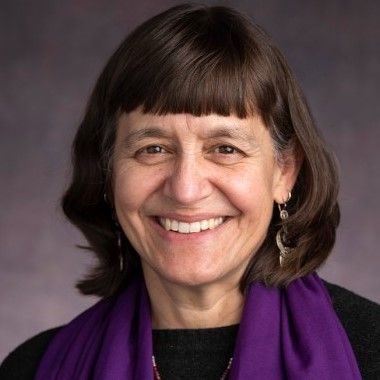 A woman wearing a purple scarf and earrings is smiling for the camera.