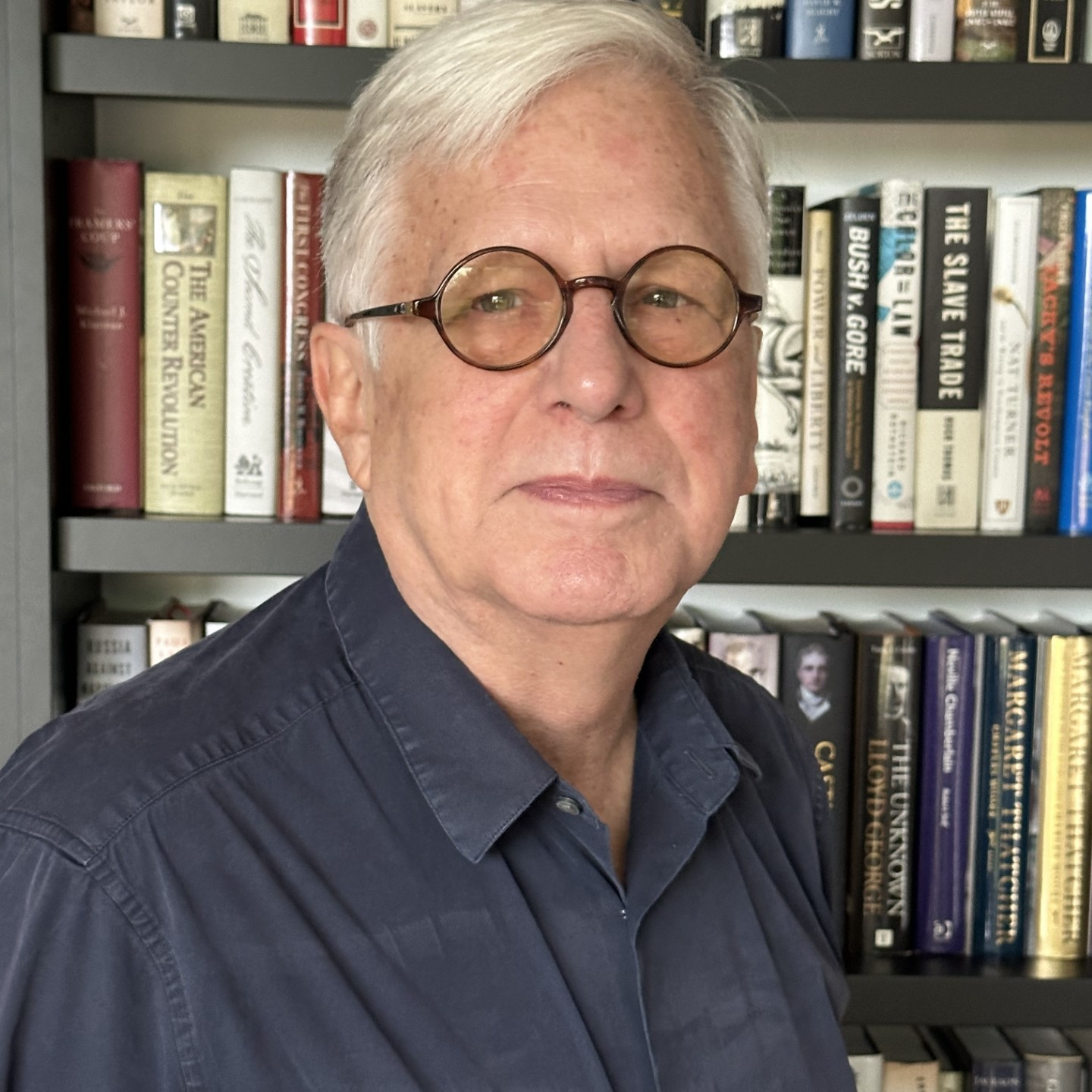 A man wearing glasses is standing in front of a bookshelf filled with books including the slave trade