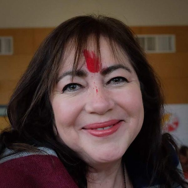 A woman with a red flower on her forehead is smiling.