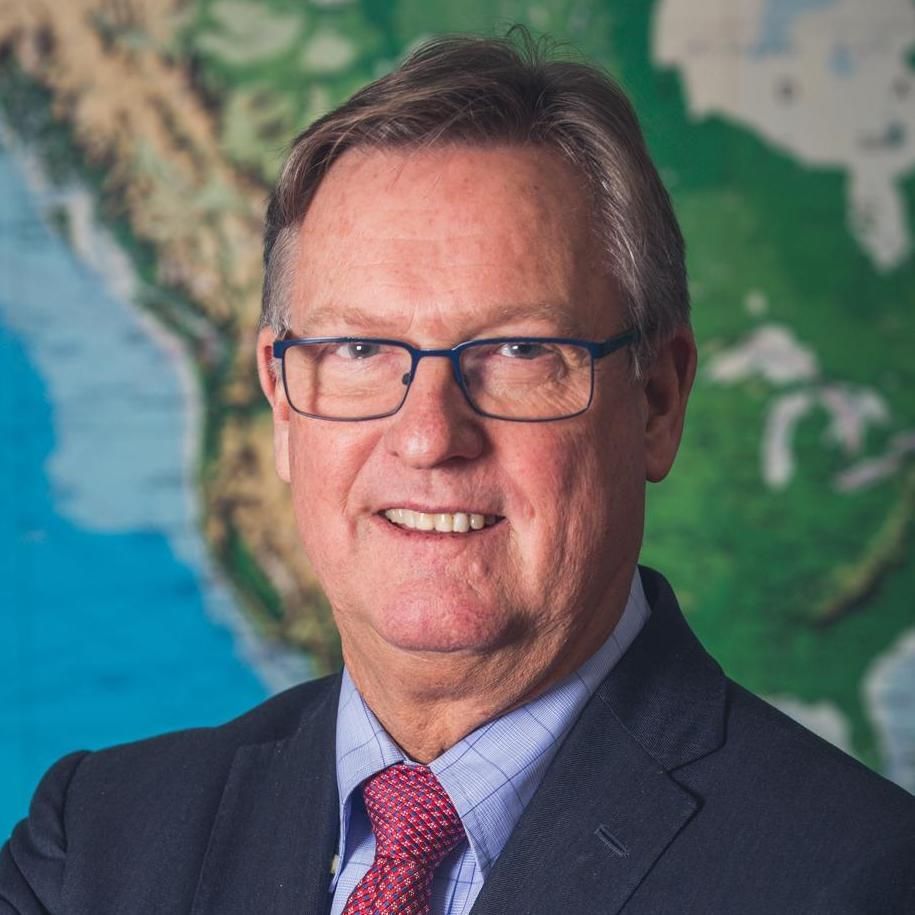 A man in a suit and tie is smiling in front of a map of the world.