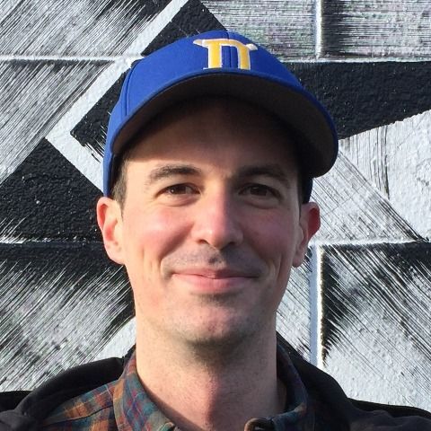 A man wearing a blue hat with the letter t on it is smiling.