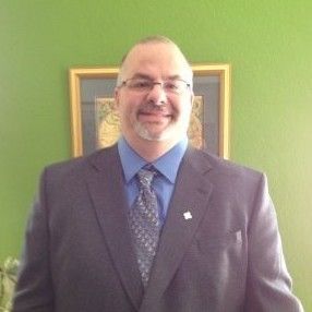 A man in a suit and tie is standing in front of a green wall.