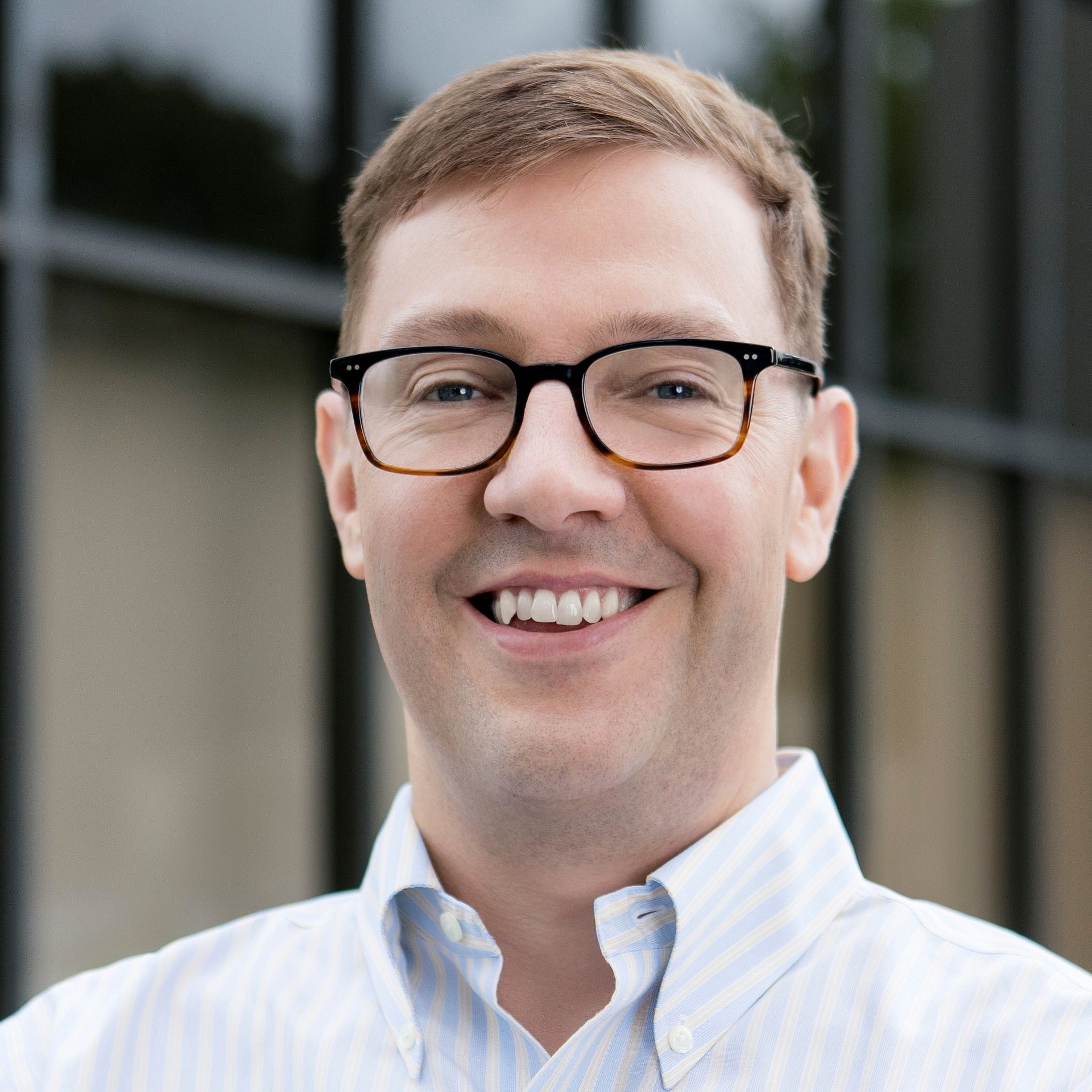 A man wearing glasses and a striped shirt is smiling for the camera.