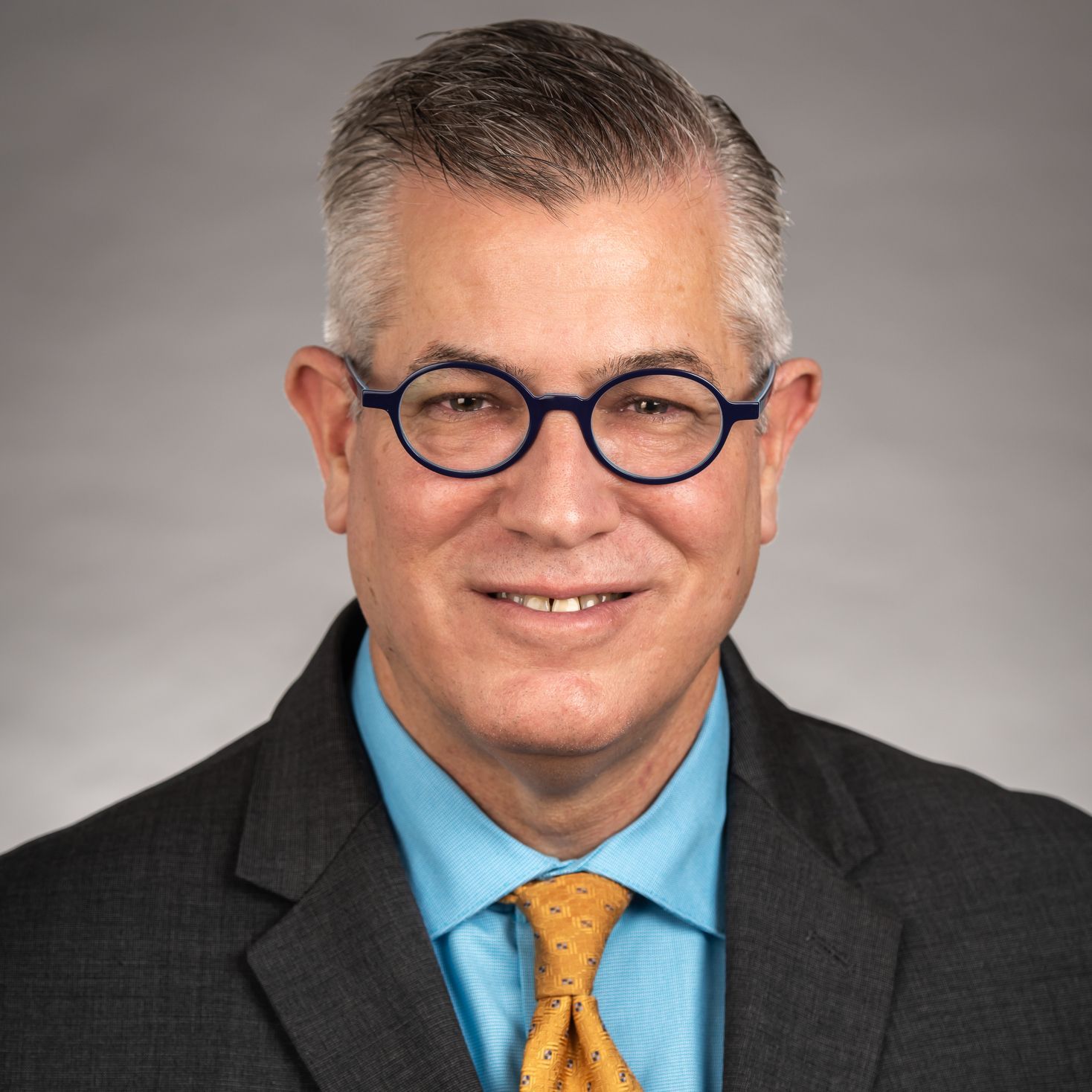 A man wearing glasses and a suit and tie is smiling for the camera.