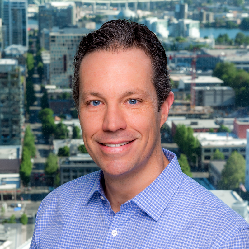 A man in a blue shirt is smiling in front of a city skyline.