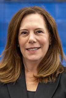 A woman with blonde hair is wearing a green sweater and a blue shirt