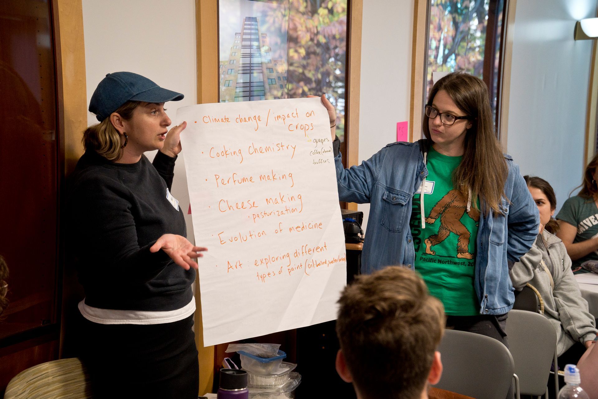 Two women are standing next to each other holding a white board.