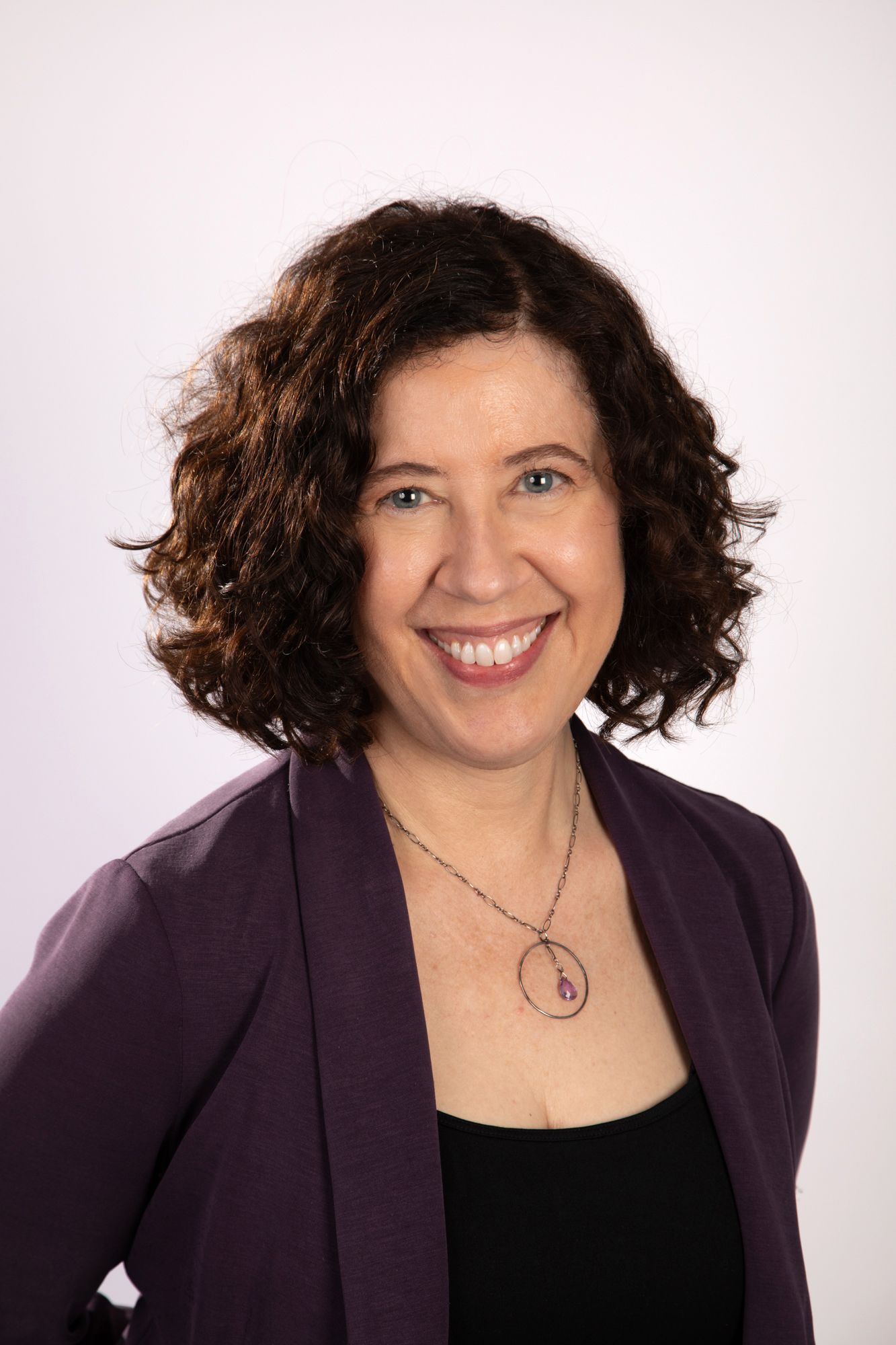 A woman wearing a maroon blazer and a necklace smiles for the camera