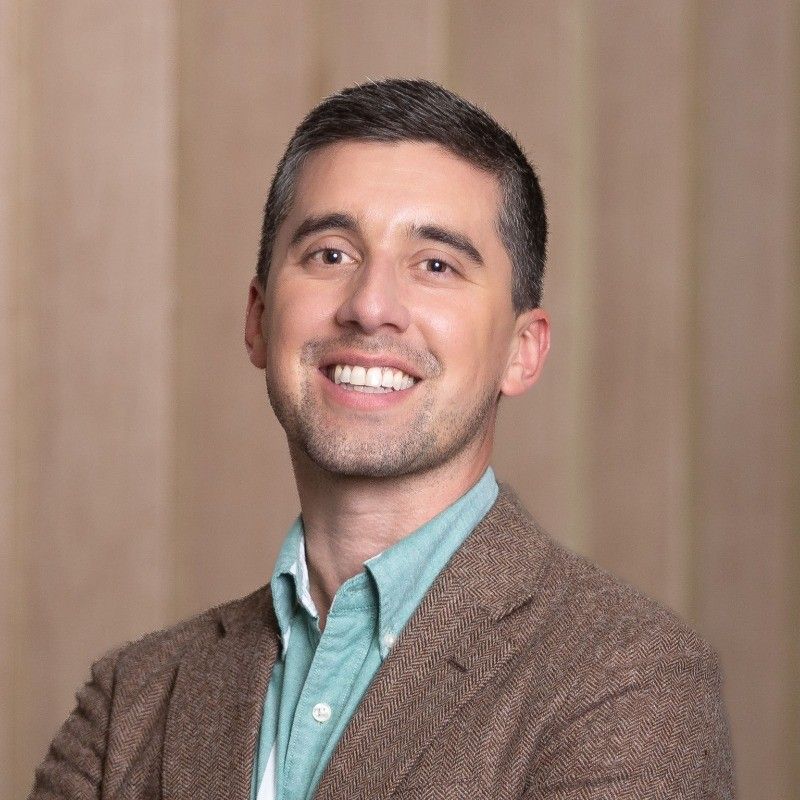 A man wearing glasses and a striped shirt is smiling for the camera.