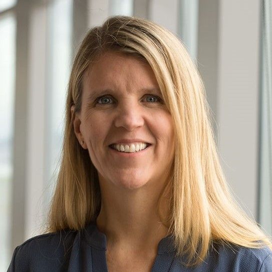 A woman with blonde hair is smiling for the camera in front of a window.