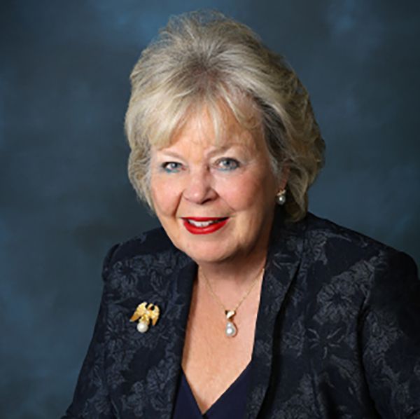 A woman wearing a black jacket and a necklace is smiling for the camera.