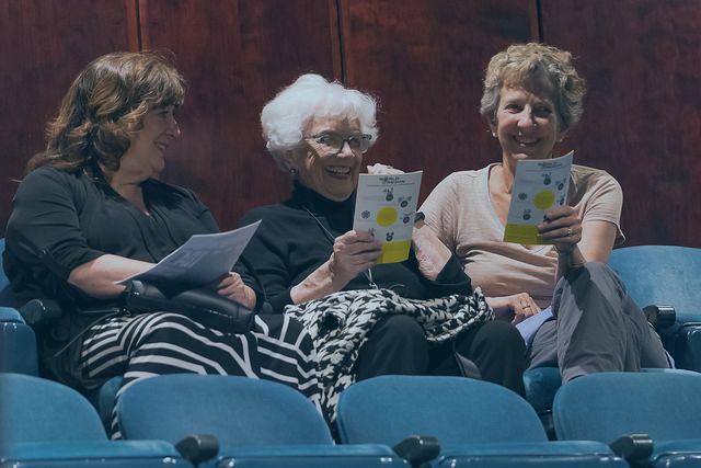 Three women are sitting in a theater holding brochures