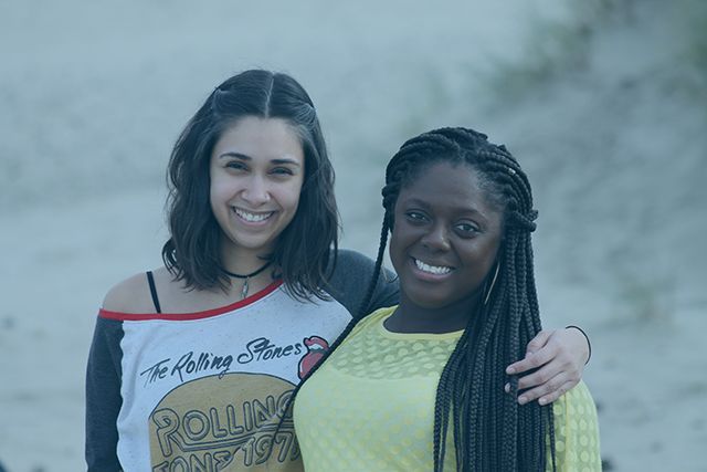 Two women are posing for a picture on the beach . one of the women is wearing a rolling stones shirt.
