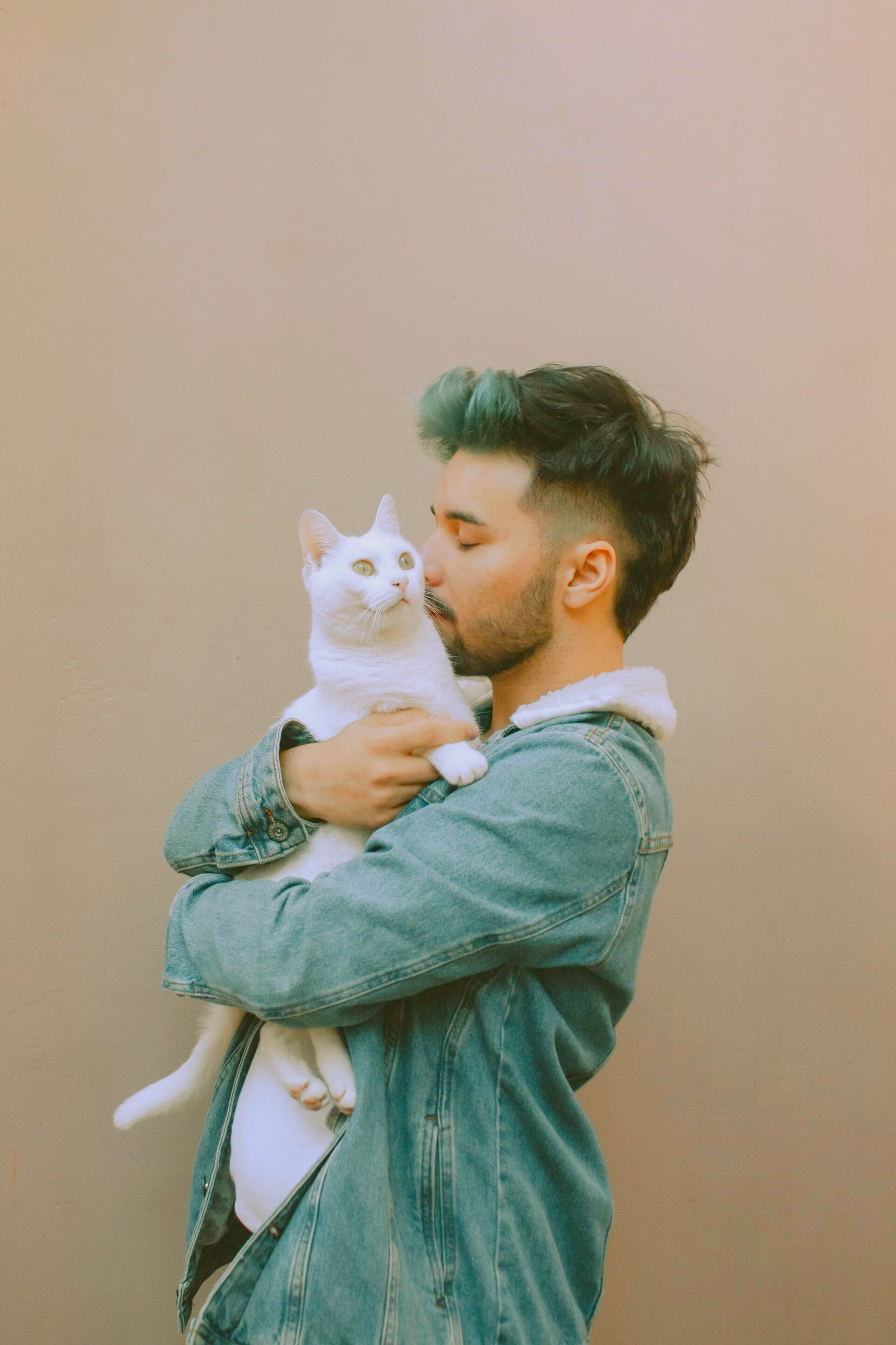 A man with green hair is holding a white cat in his arms.