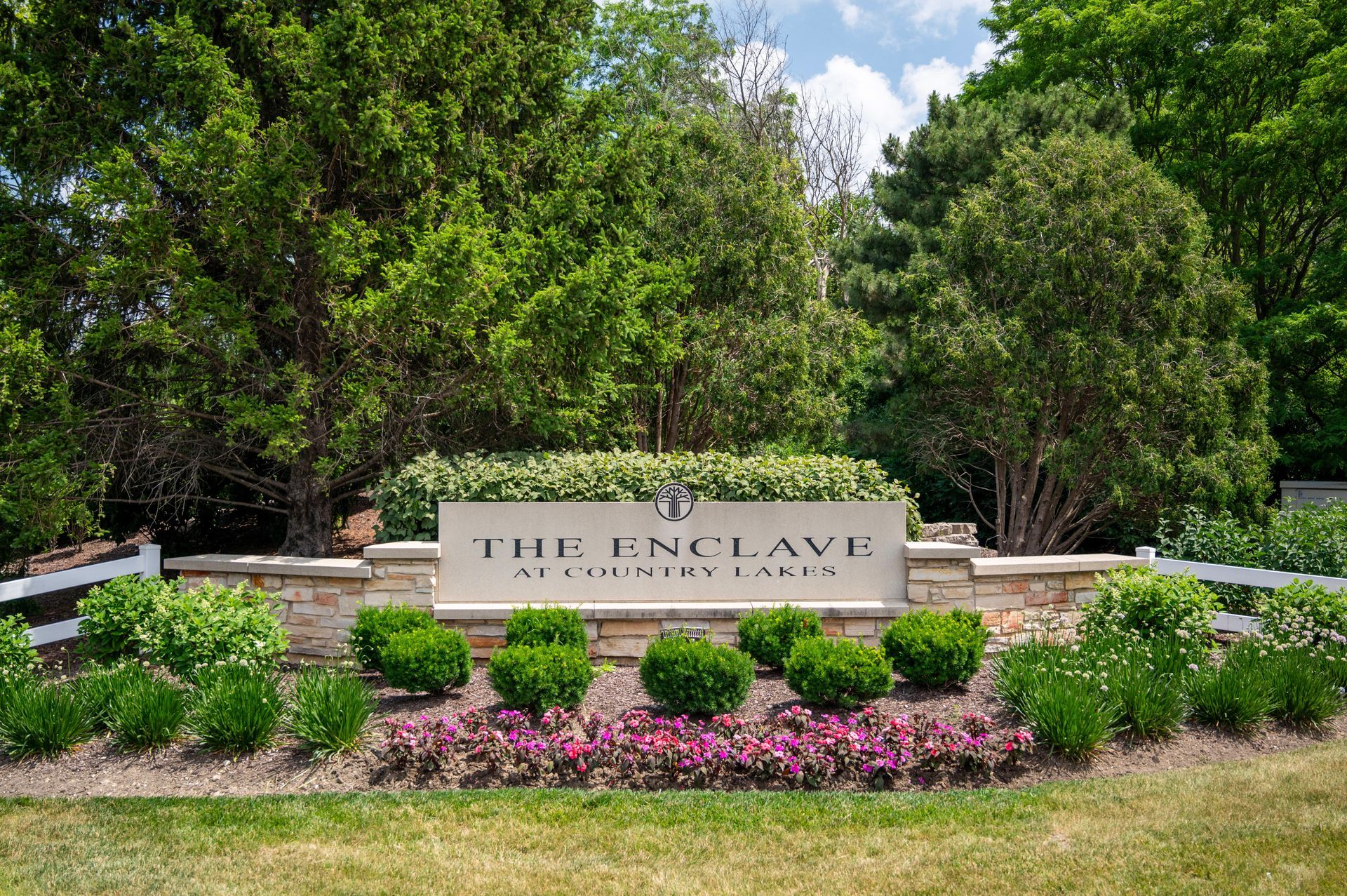 Sign for The Enclave at Country Lakes with stone structure, greenery, and bushes.