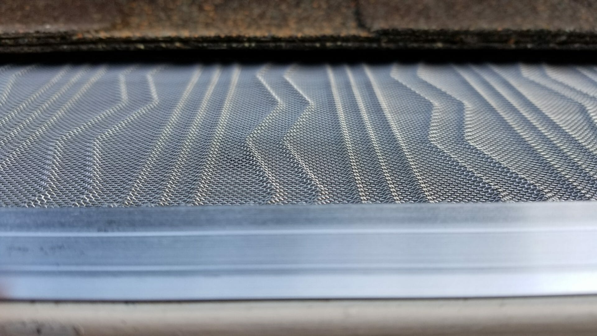 A close up of a metal gutter with a roof in the background.