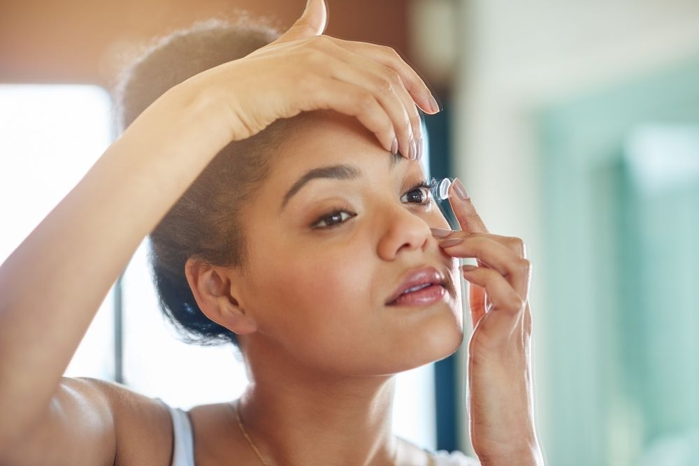 A woman is applying contact lenses to her eye in front of a mirror.