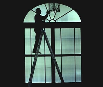 Cleaning — Silhouette of a Man Standing on a Ladder Cleaned Window in Nashville, TN