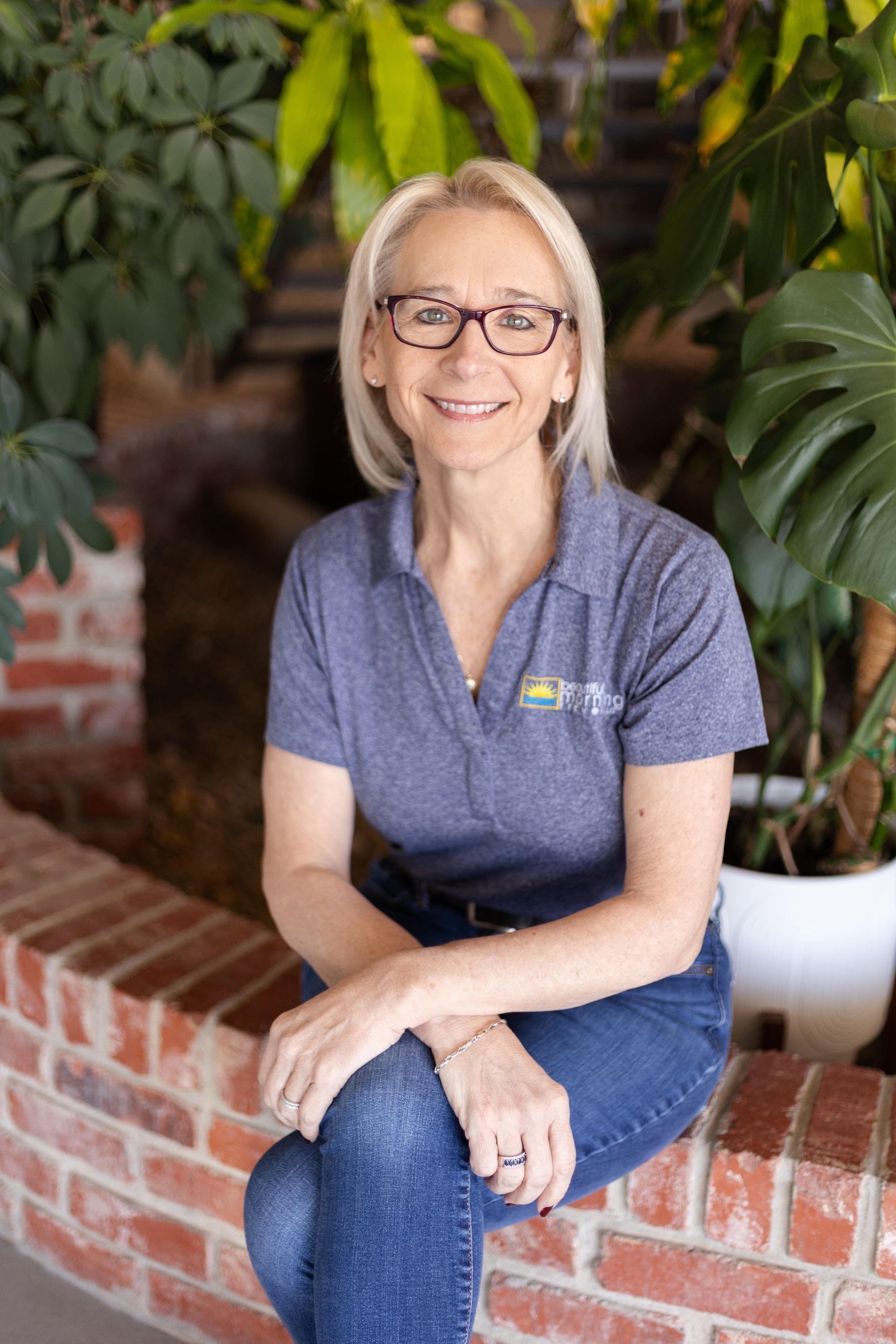 A woman wearing glasses and a denim jacket is smiling