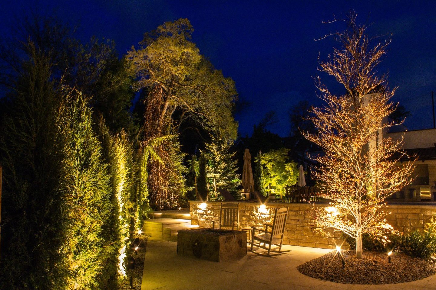 A patio area with trees and chairs lit up at night.