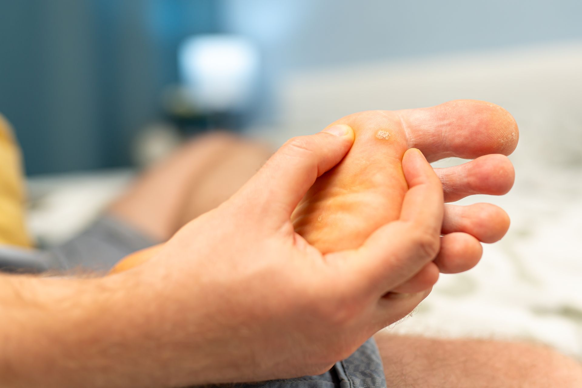 Person's hand examining foot. Foot is light-skinned with dry skin. Person is in bed with blurred background.