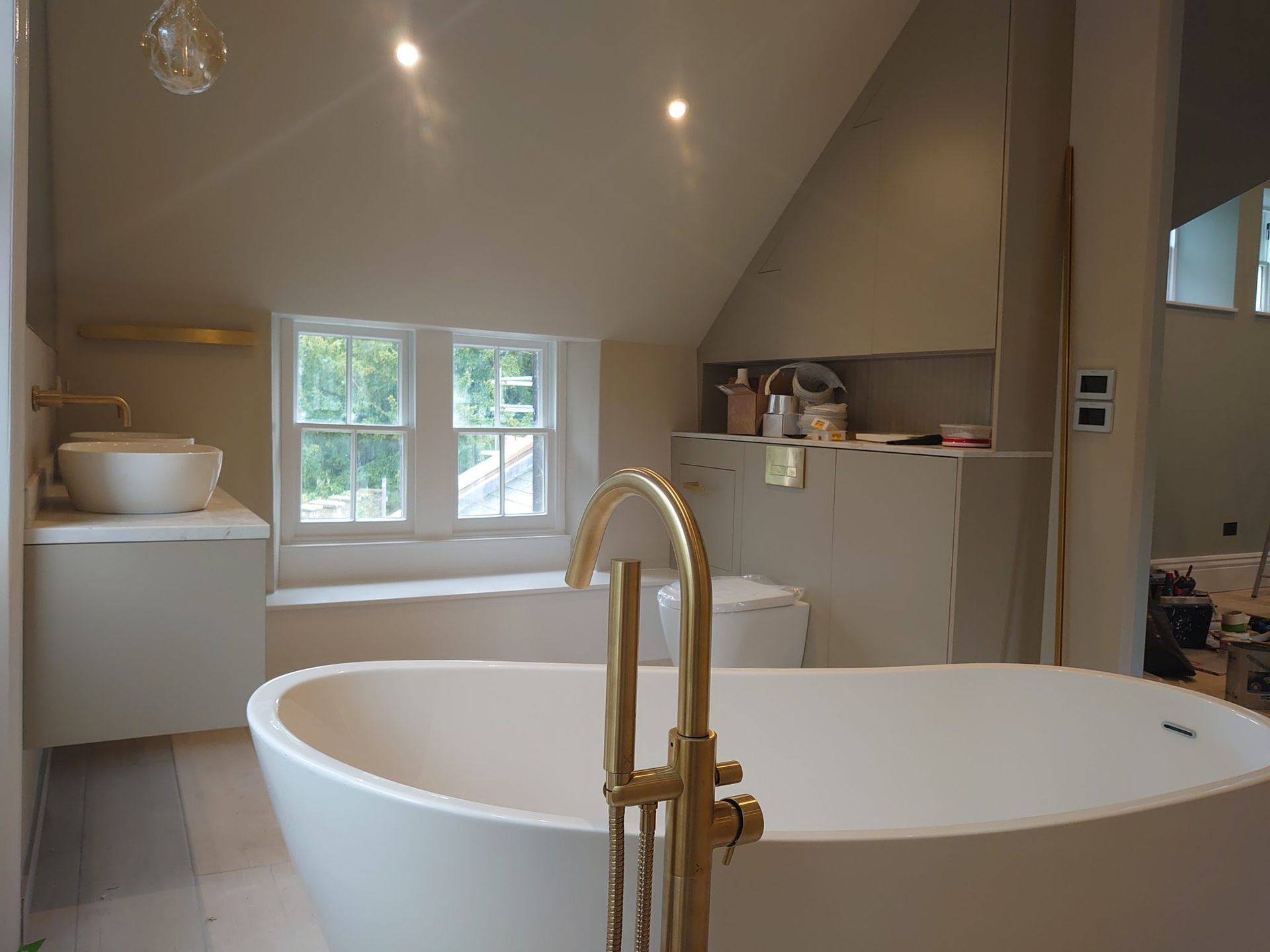 Modern bathroom with a freestanding white tub, brass faucet, white vanity sink, and a toilet under a slanted ceiling.