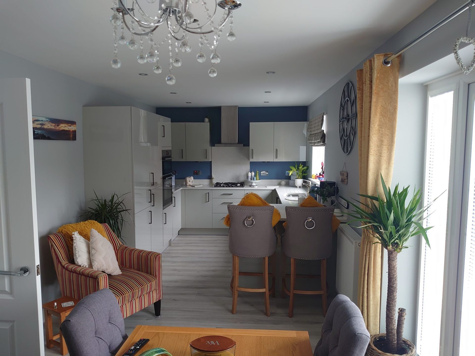 A bright open-plan kitchen and dining area featuring a crystal chandelier, modern cabinetry, and neutral seating.