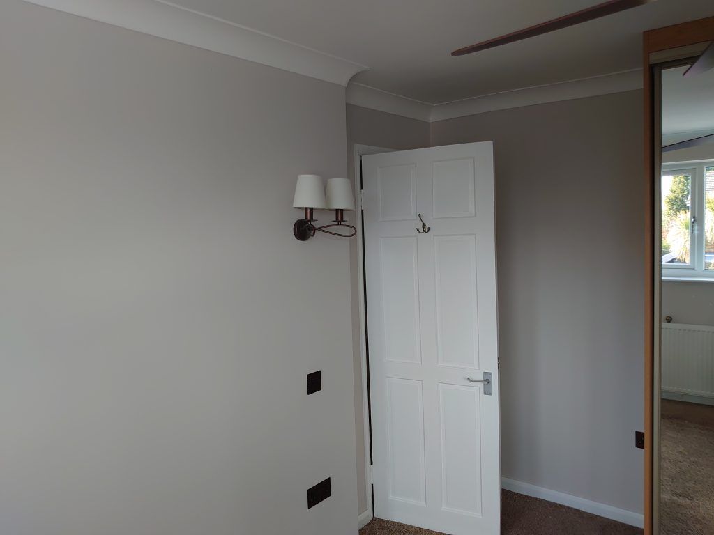A white panel door stands partially open in a room with light grey walls, a wall-mounted light fixture, and a mirror.