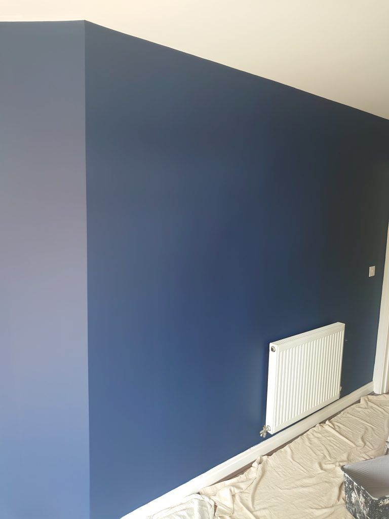 A freshly painted deep blue interior wall with a white radiator and a drop cloth on the floor.