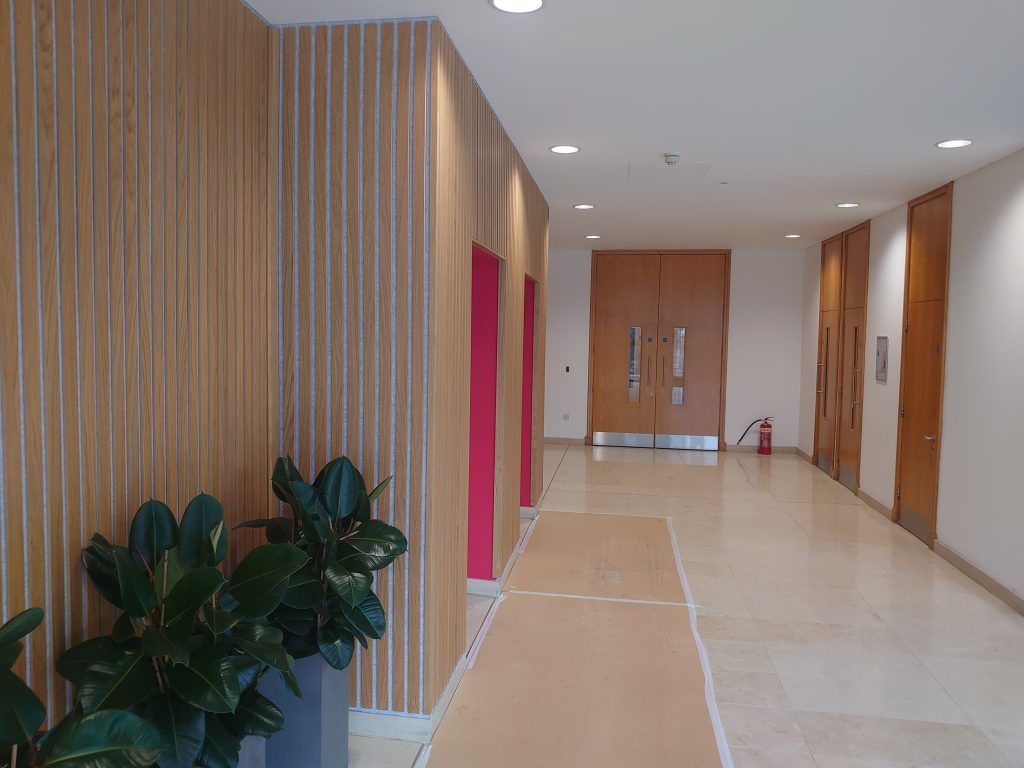 A hallway with wood-paneled walls, a light stone floor, a protective floor covering, and double wooden doors at the end.