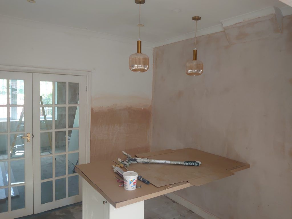 A room under renovation with fresh plaster walls, a kitchen island, and two pendant lights hanging from the ceiling.