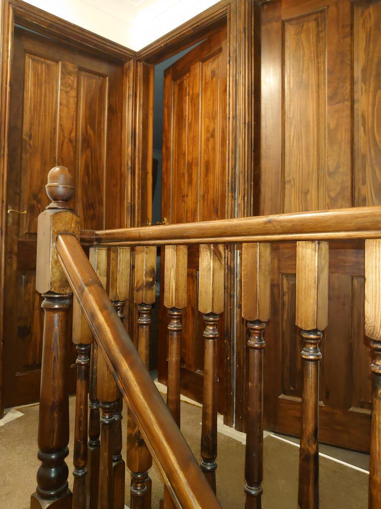 A wooden staircase banister with vertical spindles and carved posts, set against a background of matching wooden doors.