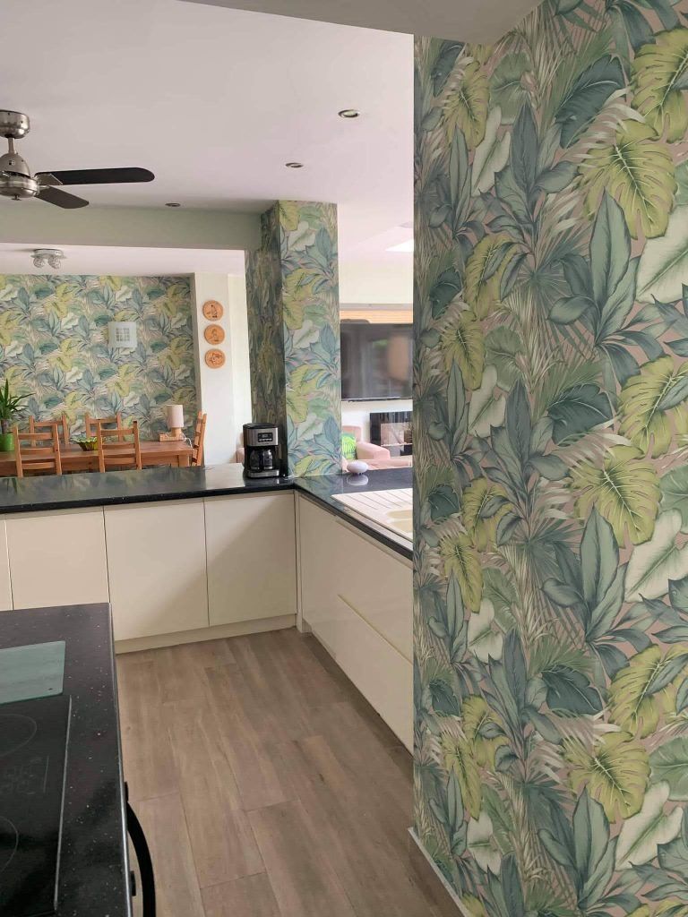 Modern kitchen and dining area featuring white cabinets, wood flooring, and tropical leaf wallpaper.