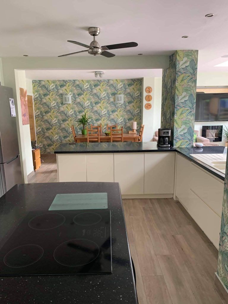 Modern kitchen with a black island countertop, white cabinets, and a dining area featuring botanical patterned wallpaper.