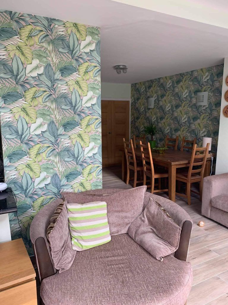 A circular mauve chair in the foreground, with tropical leaf wallpaper behind it and a wooden dining set in the distance.