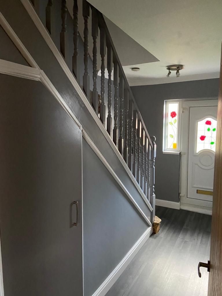 An interior hallway with a gray staircase, white trim, wood flooring, and a white front door with floral stained glass.